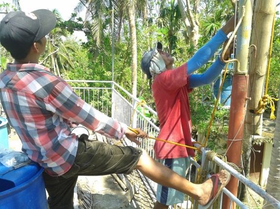 Ramir and Nho on the roof helping hoist the bamboo pole up.